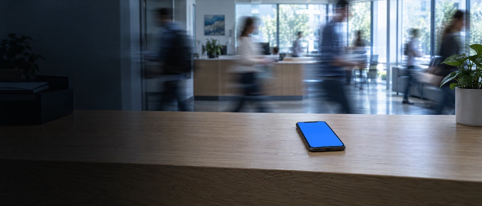 Empfangstresen in einem belebten Büro, Menschen eilen vorbei, auf dem Tresen liegt ein Smartphone